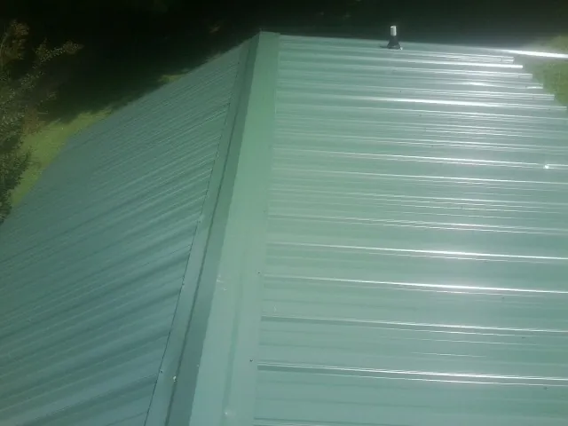 New green metal panels meeting at the ridge of a roof — Flat Roof Repair work by our crew in Ellenton