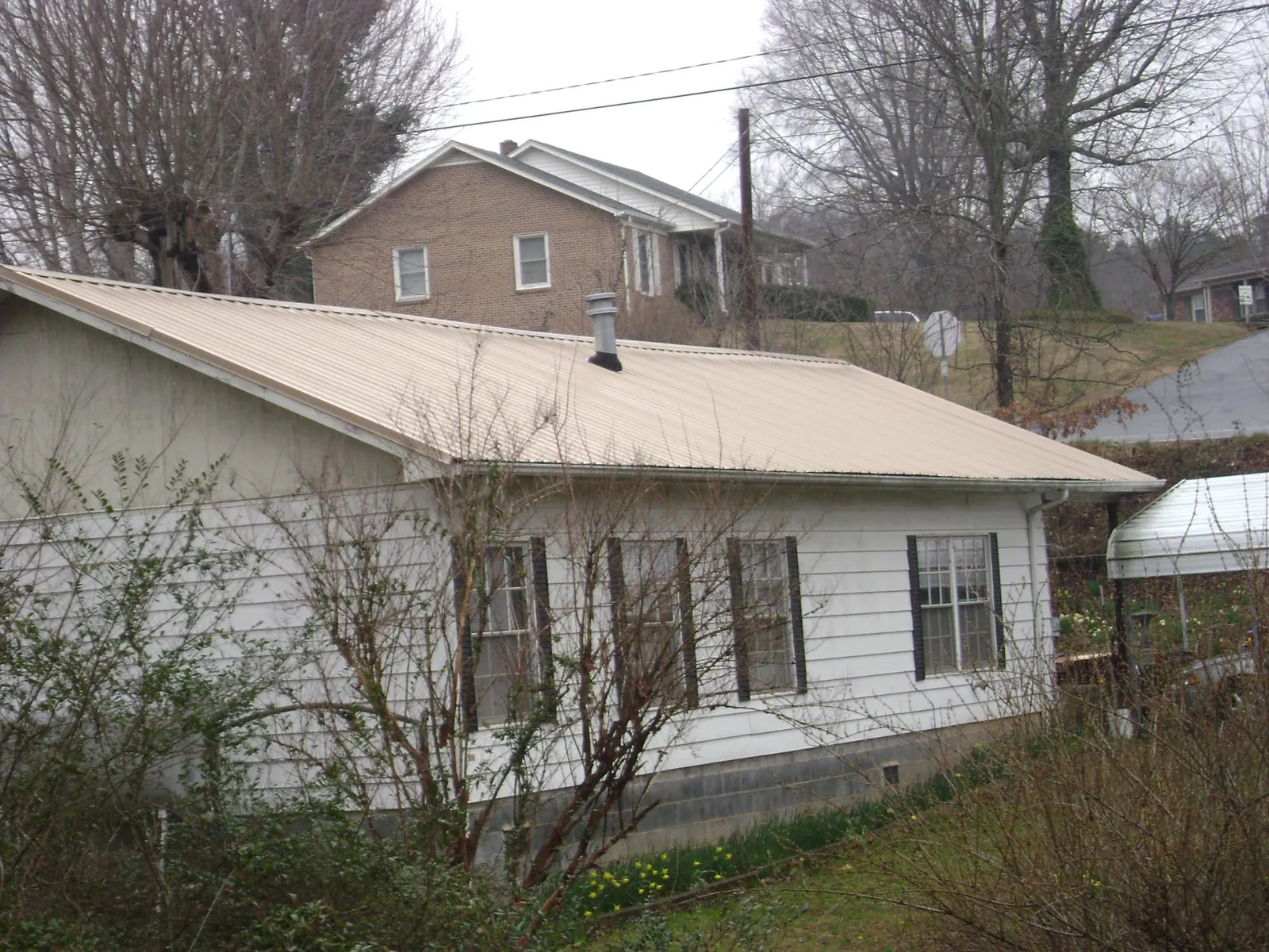 Tan metal roof on a white sided house set into a hillside — Commercial Roofing by Roofing Brothers in Ellenton